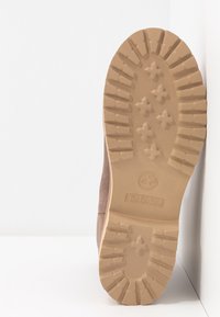 Semelle de botte Timberland avec une semelle extérieure en caoutchouc beige présentant des crampons profonds et un logo. La partie supérieure est en daim d'un ton brun clair.