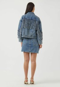 Farkkutakki, jossa pitkät hapsut takana, yhdistetty farkkuhameeseen. Vaaleansininen väri, klassinen muotoilu ja kaksi takataskua. Sileä pinta.