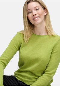 Zielony sweter dziany z okrągłym dekoltem i długimi rękawami, wykonany z miękkiego materiału. Tekstura wydaje się gładka i ciepła.
