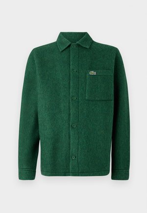 Green button-up shirt made of textured wool, featuring a collar, long sleeves, and a chest pocket with a logo.