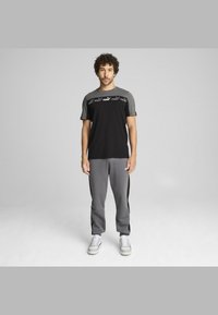 Black and gray sports outfit featuring a short-sleeve T-shirt and matching joggers, with logo detailing and side stripes. Shoes are white with gray accents.