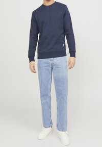 Mjörk crewneck sweatshirt med ribbad mudd och nederdel, parat med ljusblå raka denimjeans och vita sneakers. Enkel och avslappnad design.