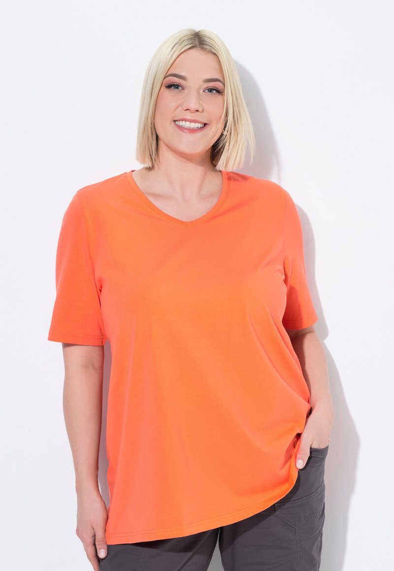 Camiseta de manga corta de color naranja brillante con escote en V, hecha de una tela suave; presenta un corte holgado y un dobladillo curvado.