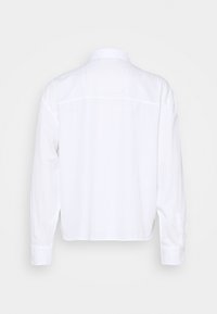 Chemise blanche à manches longues avec un col classique, une couture de empiècement au dos et des poignets boutonnés. Fabriquée dans un tissu léger avec une texture lisse.