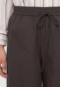Šedé lehké kalhoty s elastickým pasem a šňůrkou. Hladká textura; žádné viditelné vzory nebo kovové prvky.