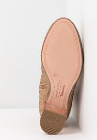 Suela de zapato marrón con textura, superficie lisa y acentos elevados. Presenta detalles de marca y talla, con un diseño de puntera redondeada.