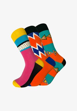 Trzy kolorowe skarpetki z geometrycznymi wzorami: różowo-żółte z czarnymi kropkami, pomarańczowo-niebieskie w zygzaki oraz morsko-zielone z pomarańczowymi trójkątami.