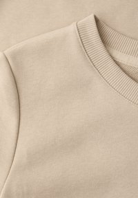 Gros plan sur un sweat-shirt en coton beige montrant l'encolure ras du cou côtelée et le détail de la couture d'épaule.