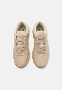 Beige treningssko med glatt lærmateriale, rund design, flate lisser og diskret merkevare på tungen. Lett såle.