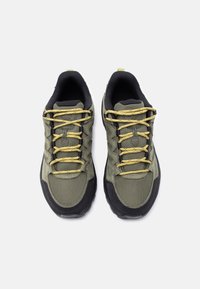 Ζευγάρι αθλητικά παπούτσια σε ελιά και μαύρο με κίτρινα κορδόνια, φωτογραφημένα από ψηλά σε λευκό φόντο.