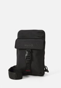 Mala pequena preta de tiracolo com aba frontal, fecho de fivela, detalhe de fecho e tira ajustável gravada com o logotipo "HUGO".