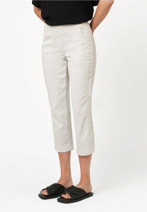 Beige Curtehose mit Fronttaschen, aus leichtem Material gefertigt. Gestickte Details verlaufen entlang der Beine, kombiniert mit schwarzen geflochtenen Sandalen.