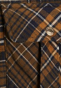 Brunt och marinblått rutigt tyg med en texturerad väv. Har vita accenter och en metallknapp med en logotyp märkt "JACK & JONES."