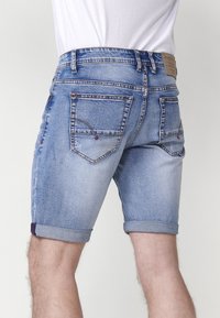 Shorts de denim azul claro con dobladillos enrollados, que cuentan con bolsillos traseros y detalles sutiles de costura. El material presenta un aspecto desgastado y deslavado.