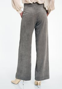 Grijze bredere corduroy broek met verticale ribbels, een hoge taille en een gladde textuur. Gepaard met beige stilettohakken.