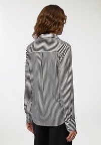 Camicia a maniche lunghe a righe bianche e nere con colletto, polsini abbottonati e dettaglio del giromanica sul retro. Tessuto liscio con righe verticali uniformi.