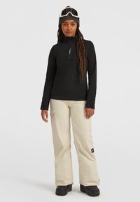 Zwarte lange mouwen zip-up top, beige cargobroek en zwarte sneeuwlaarzen. De top heeft een rits aan de voorkant en de broek heeft zijzakken.
