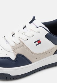 Heren sneakers in een wit, marineblauw en grijs kleurenschema. Gemaakt van leer en suède, met perforaties en witte veters. Logo detail zichtbaar.