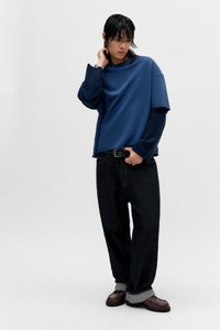 Blauer Sweatshirt mit Struktur, darüber ein dunkles Langarmshirt getragen, kombiniert mit weiten schwarzen Jeans und braunen Schuhen, die Bündchen sind hochgekrempelt.