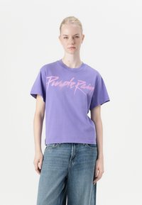 Purple cotton t-shirt with short sleeves and a crew neckline, featuring bold pink "Purple Rain" text across the front. Worn with high-waisted denim.