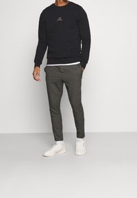 Zwarte sweatshirt met geborduurd logo, gecombineerd met broek in een ruitpatroon in donkere en lichte tinten, en witte sneakers.