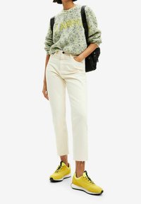 Suéter de punto verde con el texto "AWESOME" en amarillo, jeans rectos crema y zapatillas amarillas brillantes con acentos negros. Mochila negra.