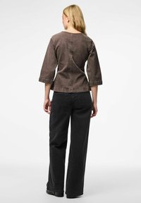 Top in denim marrone con maniche a tre quarti e scollatura rotonda. Abbinato a pantaloni neri a gamba larga con vita alta. Dettaglio di cucitura semplice.