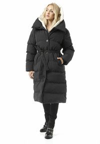 Schwarzer Steppmantel mit großem Kragen und Kapuze, ausgestattet mit einem Taillengürtel, Knopfverschluss und gesteppter Textur. Wird über dunklen Hosen getragen.