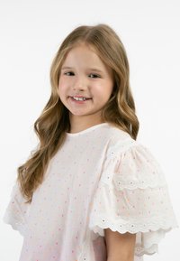 Blusa bianca con pois rosa e arancioni, maniche corte a palloncino e rifinitura in pizzo decorativo lungo le maniche e l'orlo. Tessuto morbido.