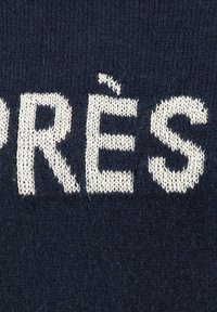 Wollstrickpullover mit cremefarbenem Text "PRÉS" auf einem dunkelblauen Hintergrund. Der Text hat eine leicht strukturierte Oberfläche im Vergleich zum glatten Stoff.