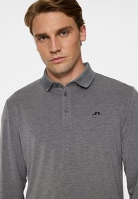 Szara koszulka polo z długim rękawem wykonana z miękkiego materiału, z kołnierzykiem, trzema guzikami i małym tłoczonym logo na piersi.