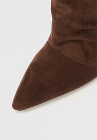 Καφέ καστόρινο μποτάκι στιλέτο με μυτερή μύτη και λεία υφή, διαθέτει εφαρμοστό άξονα και μινιμαλιστικό σχεδιασμό.