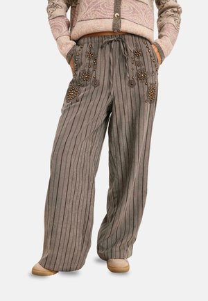 Pantalones grises con rayas sueltos con bordado floral de cuentas en los bolsillos delanteros, combinados con zapatos beige y un suéter estampado de tono rosado.
