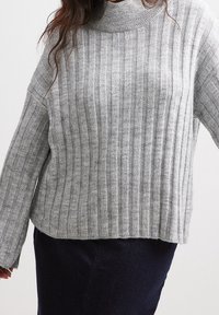 Grau gerippter Strickpullover mit hohem Kragen, weiten Ärmeln und lockerer Passform, der vertikale Streifen und eine weiche Textur aufweist.