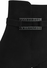 Botine negre din suede cu glezna, prezentând o curea decorativă cu accente negre dreptunghiulare. Textură netedă cu un design structurat.