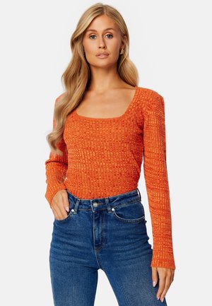 Top a maniche lunghe a coste arancione con scollo quadrato, abbinato a jeans blu a vita alta. Tessuto testurizzato con un design aderente.