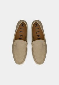 Beige suede slip-on shoes with a smooth texture, rounded toe, and visible stitching. Interior features brown insole with "HILFIGER" branding.
