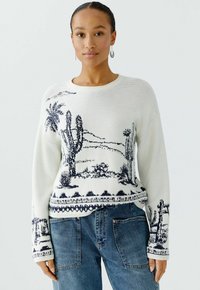 Witte gebreide trui met een blauw woestijnlandschapdesign met cactussen en palmbomen. Lange mouwen en ribgebreide zoom. Draagt deze met blauwe denimbroek.