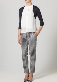 Vit blus med marinblå ärmar, knäppt framtill, tillsammans med mönstrade svartvita byxor. Grå klackar fulländar looken.