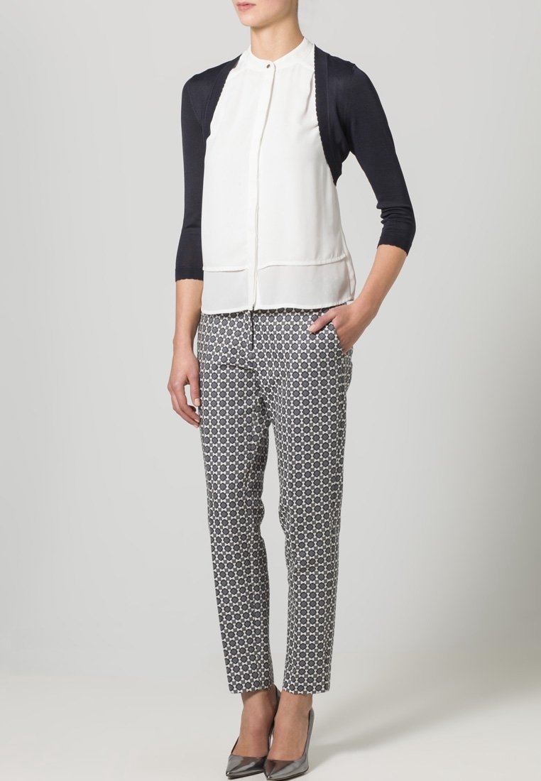 Vit blus med marinblå ärmar, knäppt framtill, tillsammans med mönstrade svartvita byxor. Grå klackar fulländar looken.