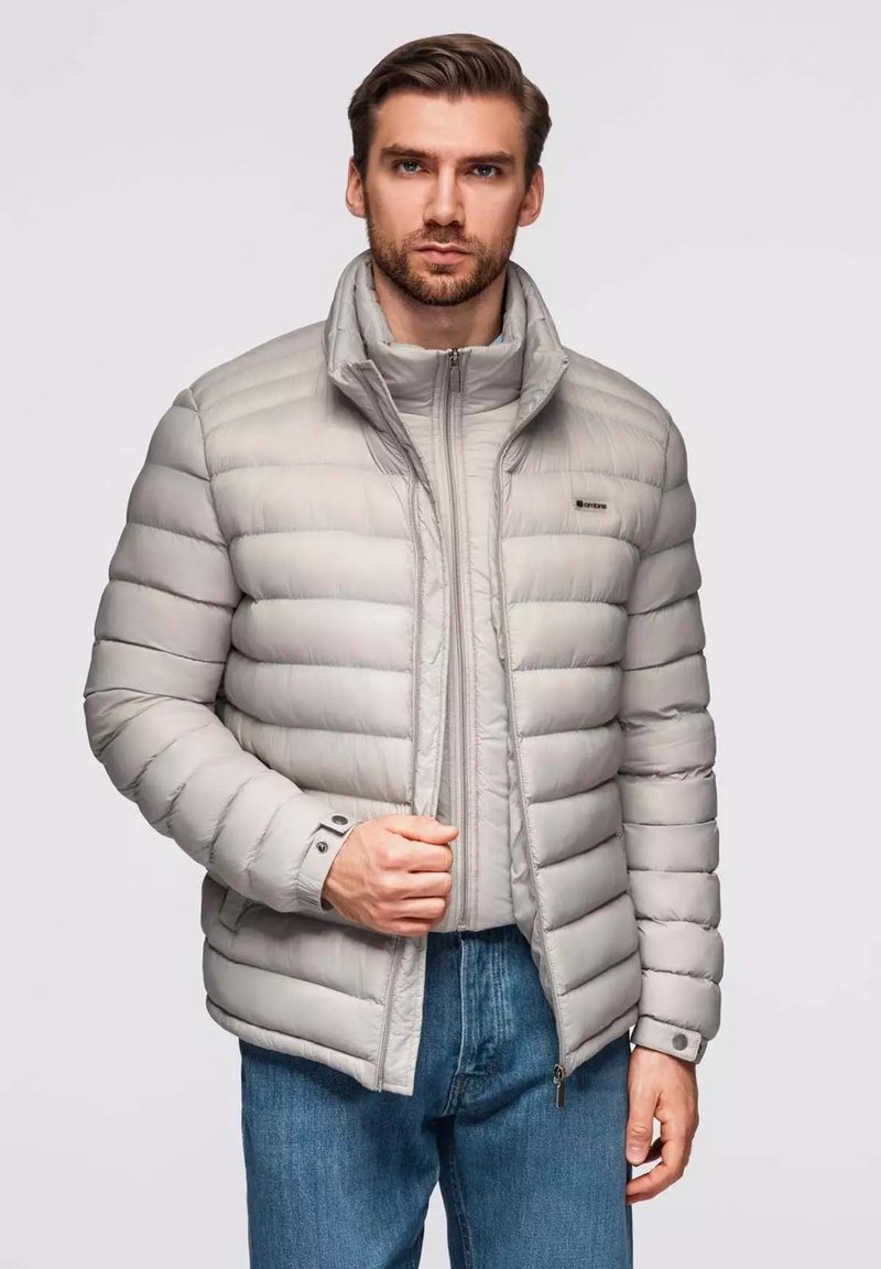 Hellgraue Pufferjacke mit zippered Front, hohem Kragen und geripptem Design. Sie hat knöpfbare Manschetten und eine lässige Passform.