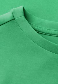 T-shirt di cotone verde con una texture liscia, scollatura rotonda e dettagli a coste. Presenta un design semplice e una colorazione uniforme.