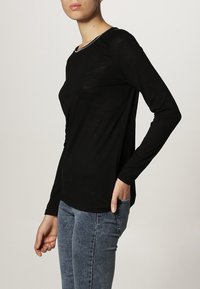 Czarna koszula z długim rękawem, okrągłym dekoltem i delikatnym połyskiem; zestawiona z jasnoniebieskimi dżinsami; dopasowany krój.