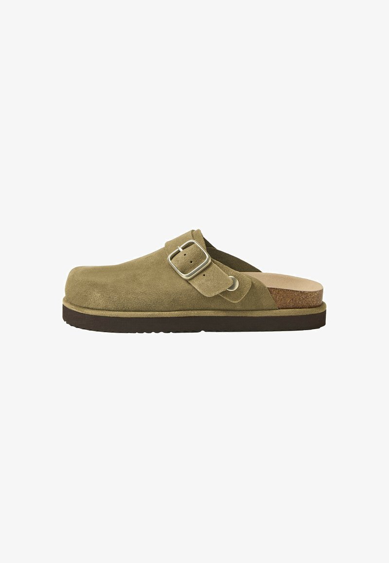 Chaussure à enfiler en suède vert olive avec une bride réglable à boucle, semelle intérieure en liège et semelle extérieure en caoutchouc foncé, vue de côté.