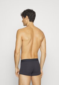 Mustat puuvillaiset boxerit, joissa on sileä rakenne ja joustava vyötärönauha, nähtynä takaa, korostaen tiukkaa istuvuutta ja minimaalista muotoilua.