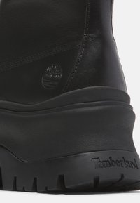 Stivale in pelle nera con suola in gomma spessa, caratterizzato da un logo in rilievo discreto e una finitura liscia. Materiale testurizzato lungo la parte superiore.