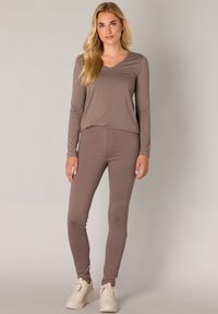 Bruine langemouwen top met V-hals en bijpassende leggings, beide gemaakt van zachte stof. Heeft een comfortabele pasvorm en subtiele stretch. Witte sneakers.