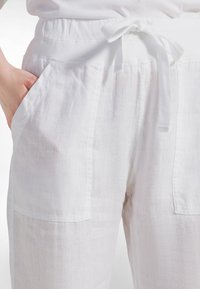 Valkoiset pellavahousut, joissa on kerätty vyötärönauha ja solmimisnauha. Housuissa on sivutaskut, teksturoitu kangas ja löysä, virtaava malli.