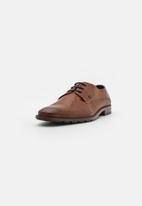 Scarpa in pelle marrone con superficie texturizzata, modello con lacci, punta arrotondata e tacco basso. Presenta lacci neri e un discreto dettaglio del logo.