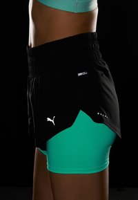 Svarta löpshorts med en teal innerfoder, elastisk midja och reflekterande "DRYCELL"-logotyp. Har en lagerdesign och Puma-logotyp.